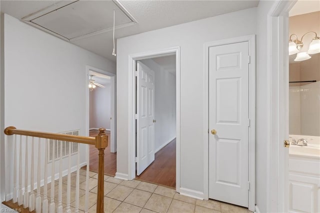 hall with light tile patterned flooring, visible vents, an upstairs landing, baseboards, and attic access