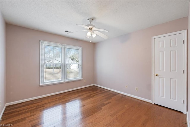 spare room with baseboards, visible vents, a ceiling fan, wood finished floors, and a textured ceiling