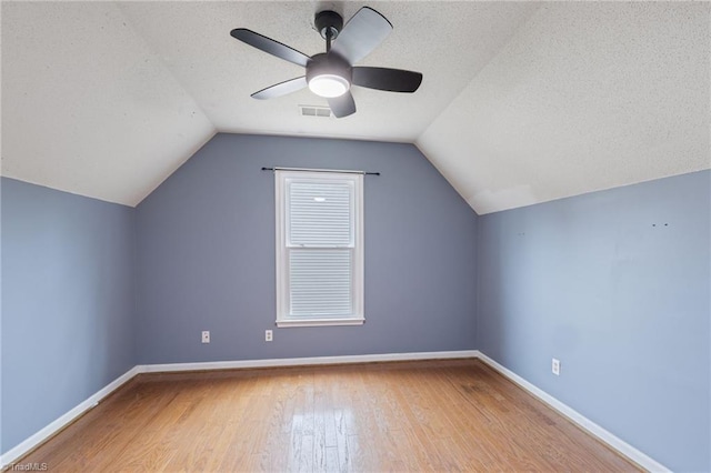 additional living space with lofted ceiling, a textured ceiling, baseboards, and wood finished floors