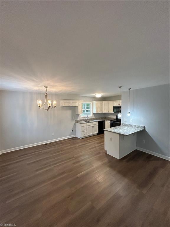 kitchen with a notable chandelier, black appliances, dark wood-type flooring, and white cabinetry