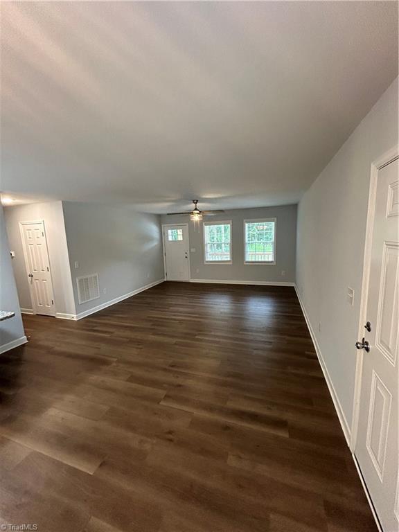 unfurnished living room with dark hardwood / wood-style flooring and ceiling fan