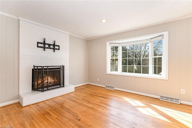 unfurnished living room featuring ornamental molding, a brick fireplace, wood finished floors, and visible vents