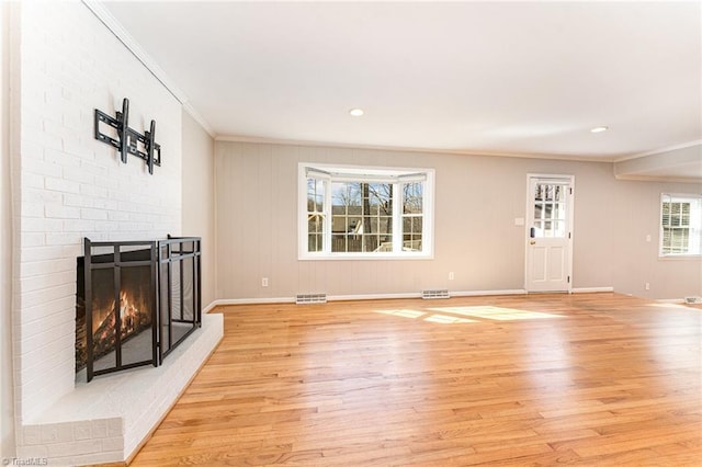 living room featuring light wood finished floors, a fireplace, visible vents, and crown molding