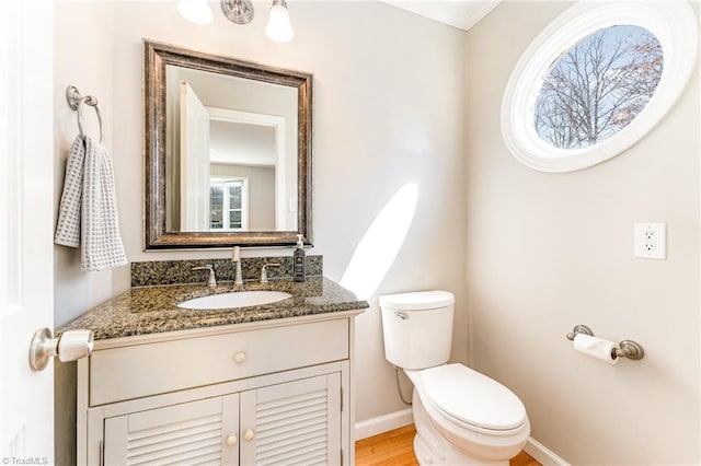 half bathroom featuring wood finished floors, vanity, toilet, and baseboards