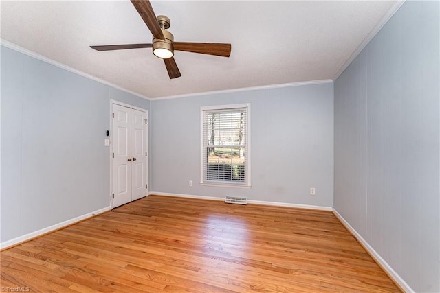 spare room with ceiling fan, light wood-style flooring, visible vents, baseboards, and ornamental molding