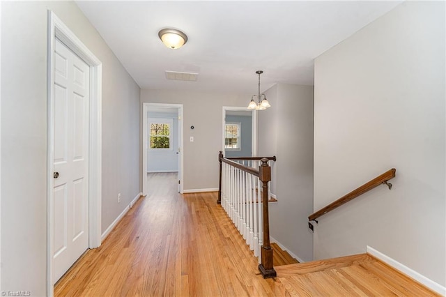 hall with visible vents, light wood-type flooring, an upstairs landing, and baseboards