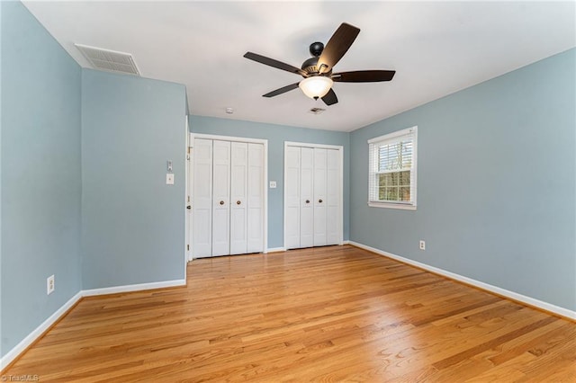 unfurnished bedroom with light wood-style flooring, two closets, visible vents, and baseboards