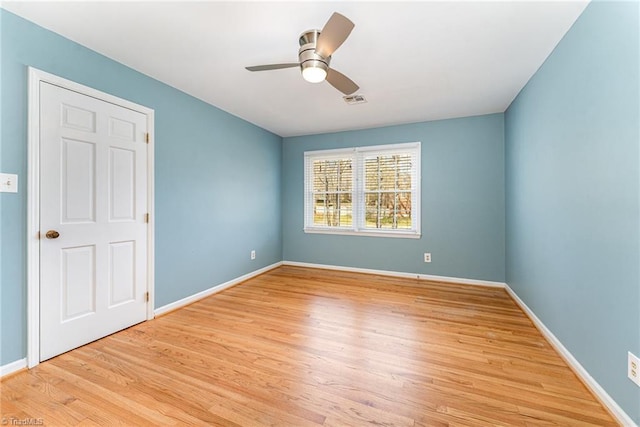 empty room featuring ceiling fan, visible vents, baseboards, and wood finished floors