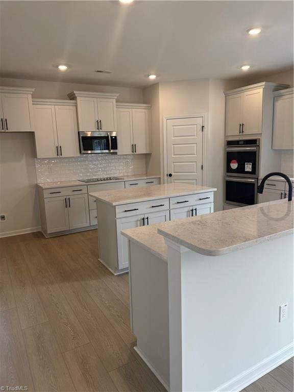 kitchen with appliances with stainless steel finishes, white cabinetry, a center island, tasteful backsplash, and light hardwood / wood-style floors