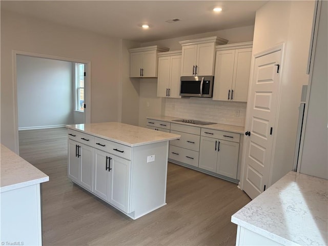 kitchen featuring tasteful backsplash, white cabinets, a center island, black electric stovetop, and light wood-type flooring