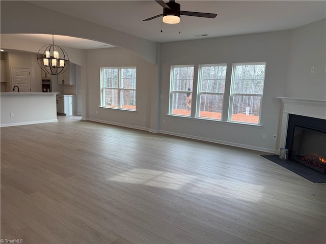 unfurnished living room featuring ceiling fan with notable chandelier and light hardwood / wood-style floors