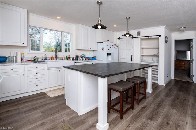 kitchen featuring white cabinets, a kitchen island, white refrigerator with ice dispenser, and pendant lighting