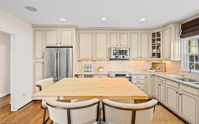 kitchen with sink, appliances with stainless steel finishes, cream cabinets, light hardwood / wood-style floors, and decorative backsplash