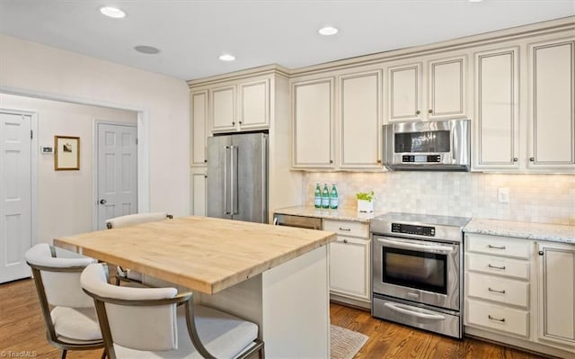 kitchen featuring hardwood / wood-style flooring, appliances with stainless steel finishes, a center island, decorative backsplash, and cream cabinetry