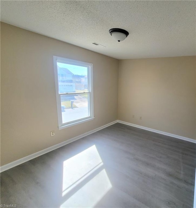 spare room featuring a textured ceiling, dark wood-type flooring, and baseboards