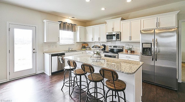 kitchen featuring appliances with stainless steel finishes, a breakfast bar, white cabinets, a center island, and light stone counters