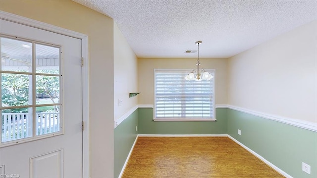 unfurnished dining area featuring wood-type flooring, a textured ceiling, and an inviting chandelier