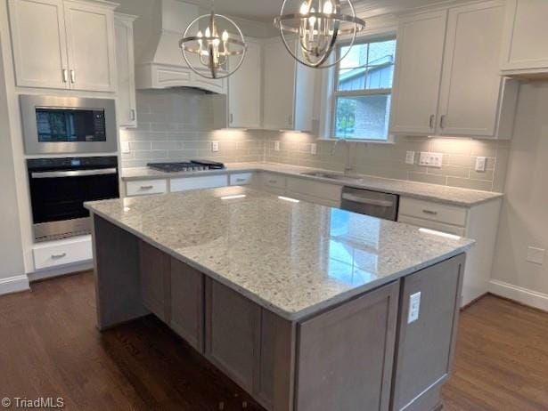 kitchen with a sink, dark wood-style flooring, stainless steel appliances, a notable chandelier, and custom exhaust hood