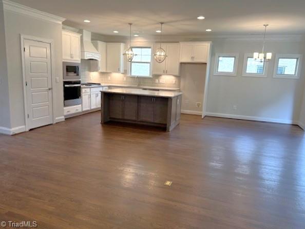 kitchen featuring custom range hood, an inviting chandelier, oven, built in microwave, and ornamental molding