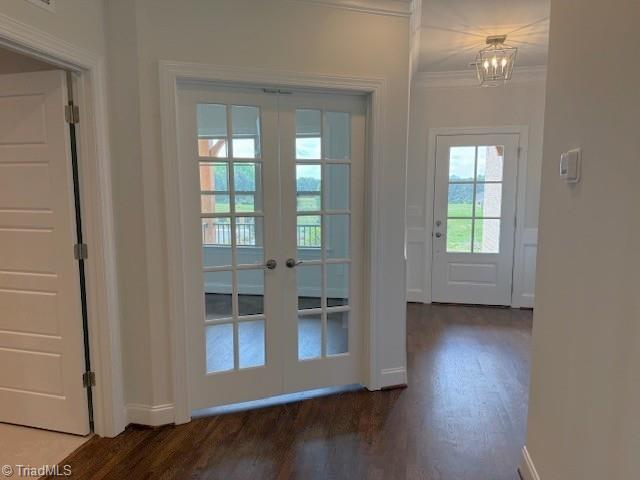 doorway to outside featuring crown molding, dark wood-style floors, baseboards, an inviting chandelier, and french doors
