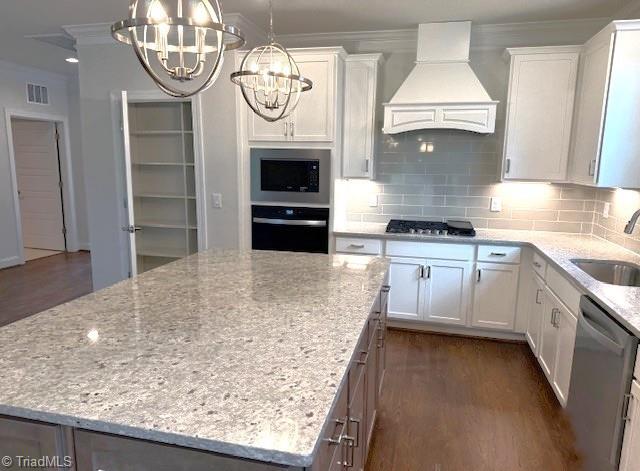 kitchen featuring appliances with stainless steel finishes, visible vents, premium range hood, a center island, and an inviting chandelier