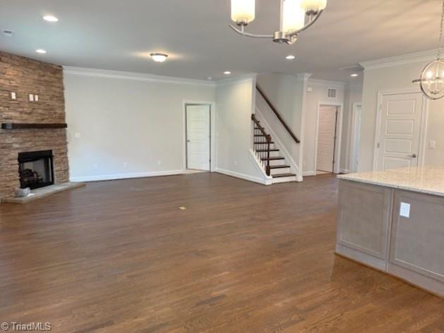 unfurnished living room featuring crown molding, dark wood-style floors, an inviting chandelier, a stone fireplace, and stairs