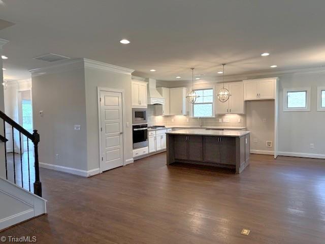 kitchen with appliances with stainless steel finishes, ornamental molding, custom range hood, and baseboards