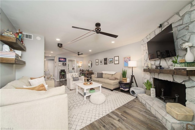 living area with wood finished floors, a ceiling fan, a stone fireplace, and recessed lighting