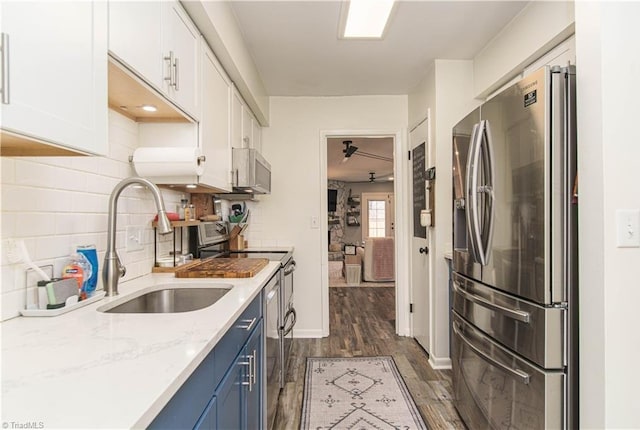 kitchen featuring appliances with stainless steel finishes, a sink, blue cabinetry, dark wood-style floors, and white cabinets