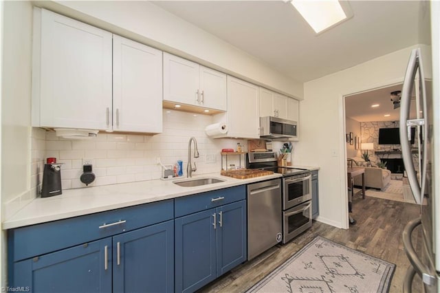 kitchen with a sink, appliances with stainless steel finishes, blue cabinets, white cabinets, and tasteful backsplash