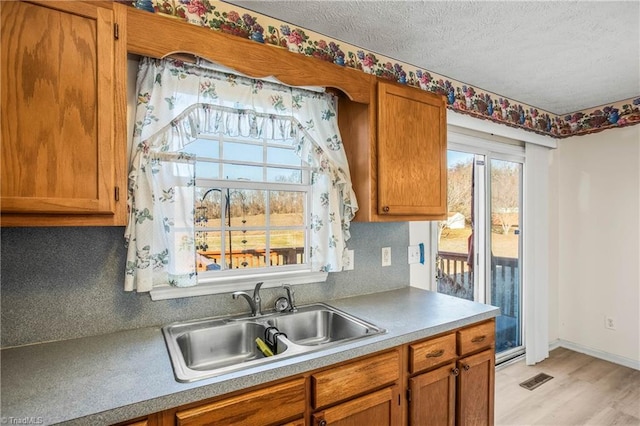 kitchen featuring a textured ceiling, light wood-type flooring, backsplash, and sink