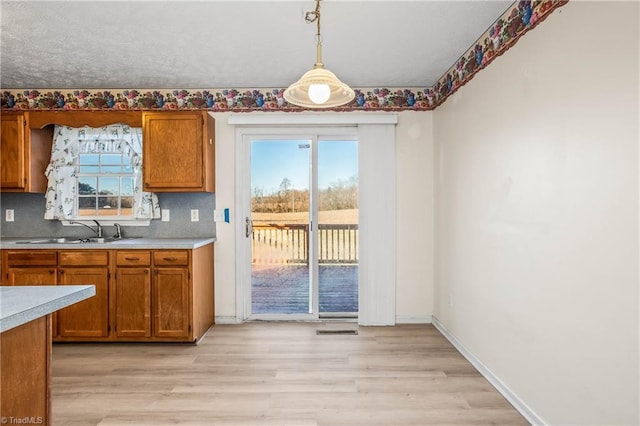 kitchen with decorative backsplash, pendant lighting, light wood-type flooring, and sink