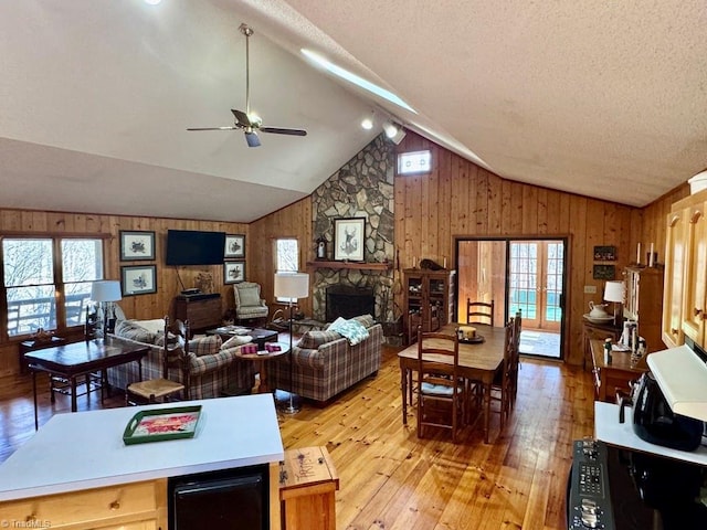 living room with vaulted ceiling, ceiling fan, light hardwood / wood-style flooring, a fireplace, and wood walls