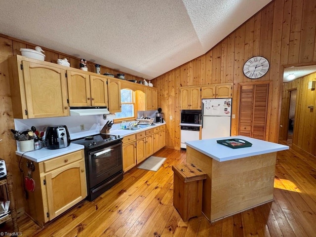 kitchen with wood walls, light hardwood / wood-style floors, vaulted ceiling, a kitchen island, and black appliances