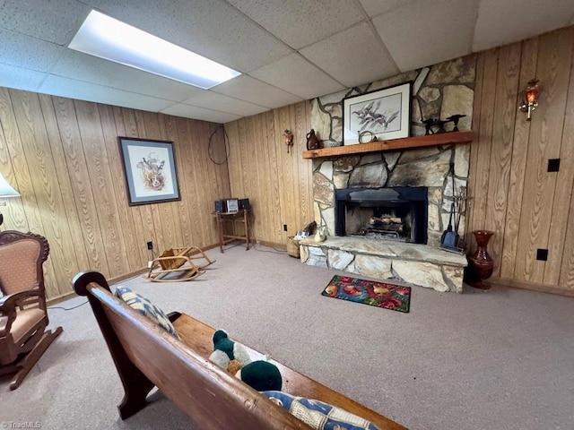 carpeted living room featuring a drop ceiling, wood walls, and a fireplace