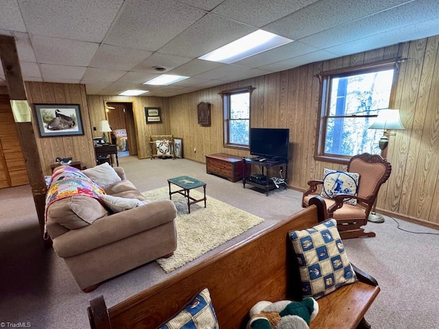 living room featuring carpet flooring, a paneled ceiling, wooden walls, and a wealth of natural light