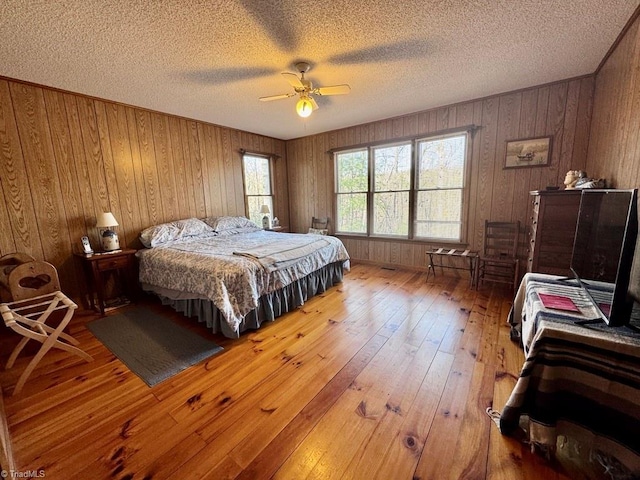 bedroom with hardwood / wood-style flooring, ceiling fan, a textured ceiling, and wooden walls