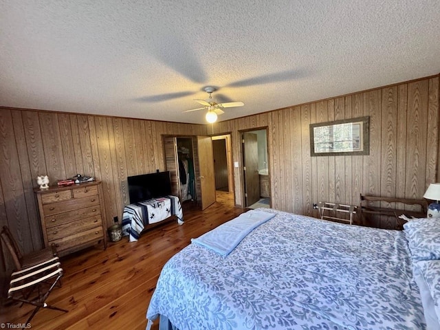 bedroom with a textured ceiling, ceiling fan, dark wood-type flooring, and wooden walls