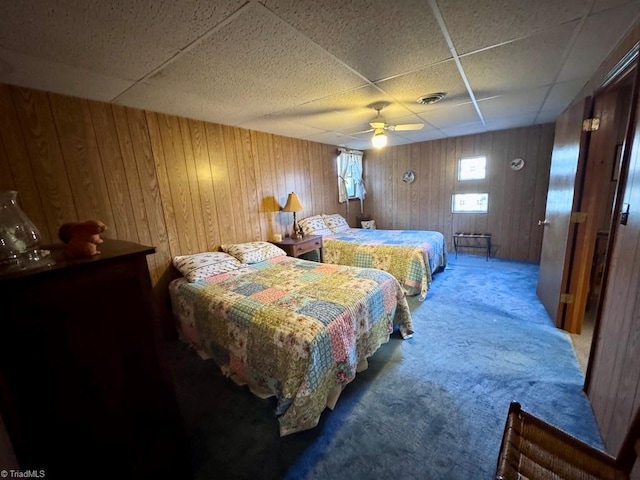 carpeted bedroom with ceiling fan, a drop ceiling, and wooden walls