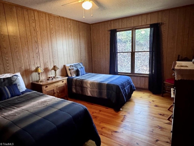 bedroom with ceiling fan, light wood-type flooring, a textured ceiling, and wooden walls