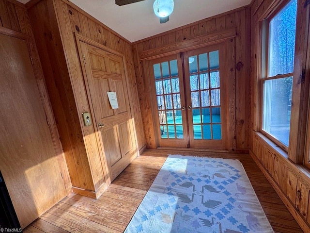 doorway to outside with wooden walls, french doors, ceiling fan, and light hardwood / wood-style floors