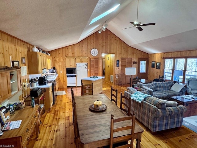 dining area featuring wooden walls, light hardwood / wood-style flooring, and lofted ceiling with skylight