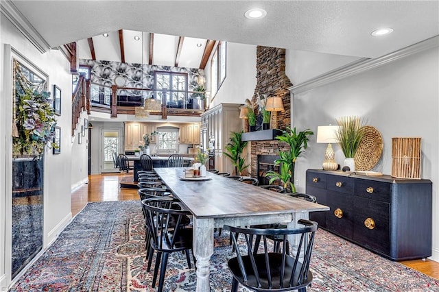 dining area featuring crown molding, a stone fireplace, light hardwood / wood-style flooring, and a high ceiling