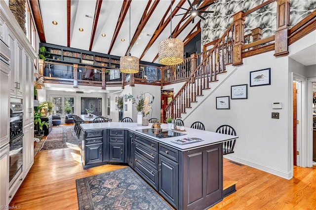 kitchen with beam ceiling, a towering ceiling, a center island, and light wood-type flooring