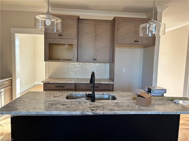 kitchen with tasteful backsplash, light stone countertops, ornamental molding, hanging light fixtures, and a sink