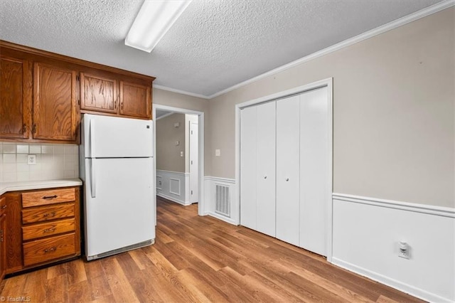 kitchen featuring light wood-style flooring, light countertops, ornamental molding, a textured ceiling, and freestanding refrigerator