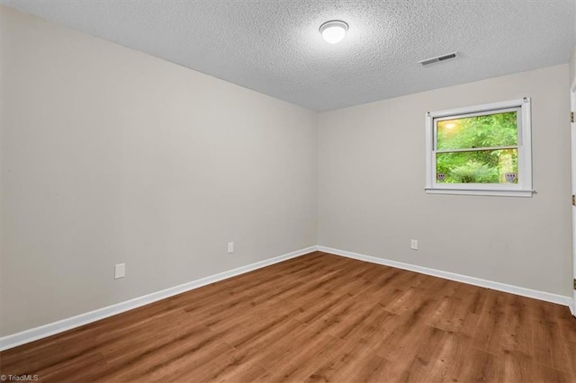 spare room with a textured ceiling, visible vents, wood finished floors, and baseboards