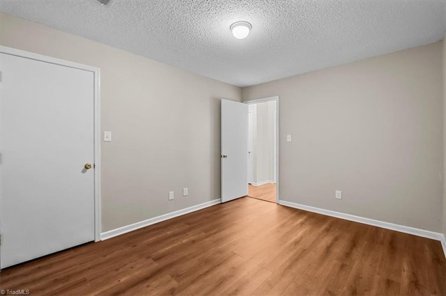 unfurnished bedroom with a textured ceiling, wood finished floors, and baseboards