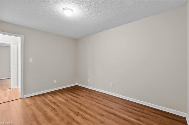 empty room featuring baseboards, a textured ceiling, and light wood finished floors