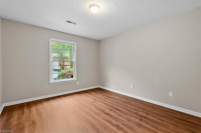 spare room featuring wood finished floors, visible vents, a textured ceiling, and baseboards
